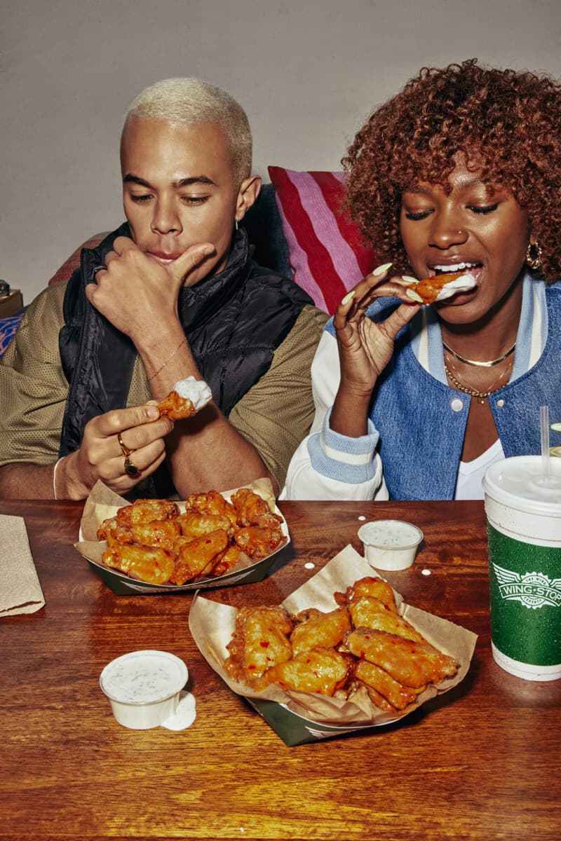 Two people sharing sauced Wingstop wings at a table
